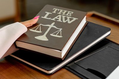 Closeup image of a law book titled 'The Law' on a wooden desk with scales of justice.